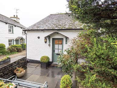 An entrance to a white house with a green door surrounded by plants and flowers at Syke Cottage in Hawkshead