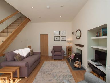 A living room with a sofa armchair rug fireplace recessed shelves and wooden stairs at Mylnbeck in Bowness