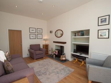 A living room with two armchairs a sofa a rug a fireplace and a built-in shelving unit at Mylnbeck in Bowness