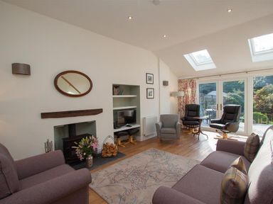 A living room with sofas armchairs a fireplace and glass doors to a garden at Mylnbeck in Bowness