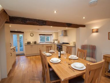 A kitchen and dining area with a wooden table set with plates and glasses and kitchen cabinets and appliances at Mylnbeck in Bowness