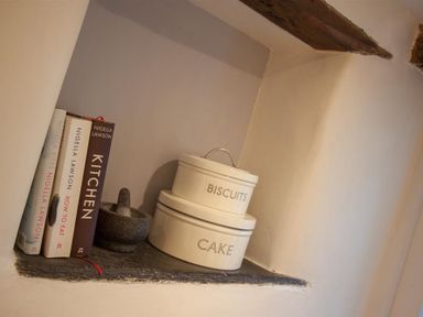 A kitchen shelf with cookbooks a mortar and pestle and containers labeled biscuits and cake at Mylnbeck in Bowness