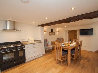 A kitchen and dining area with wooden table and chairs a stove and armchairs at Mylnbeck in Bowness