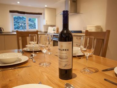 A dining table set with a bottle of malbec wine plates bowls cutlery and wine glasses in a kitchen at Mylnbeck in Bowness