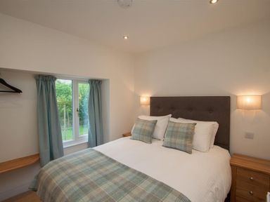 A bedroom with a bed with plaid pillows and blanket two wall lights a window with curtains and a wooden nightstand at Mylnbeck in Bowness