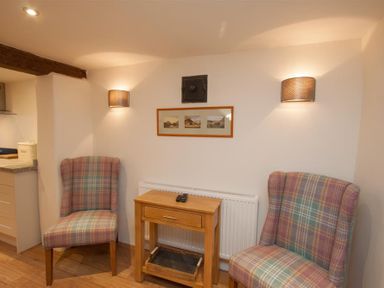 Two plaid upholstered chairs with a small wooden table between them against a white wall with framed pictures and wall lights at Mylnbeck in Bowness