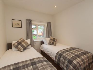 A bedroom with two single beds with plaid blankets and pillows a window with curtains and a framed picture on the wall at Mylnbeck in Bowness