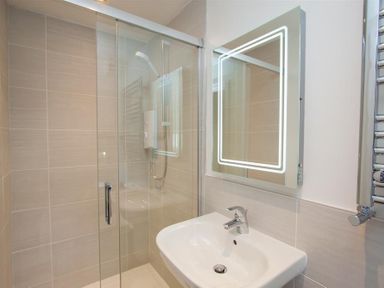 A bathroom with a shower enclosure a sink a lit rectangular mirror and a towel radiator at Mylnbeck in Bowness