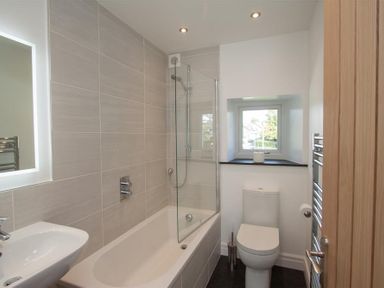 A bathroom with a bathtub shower combination a toilet a sink and a window at Mylnbeck in Bowness