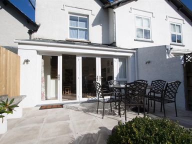 A patio with a table and six chairs outside a white house with glass doors at Mylnbeck in Bowness