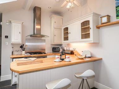A kitchen with wooden countertops white cabinets and two white stools at Hazeldene in Ambleside