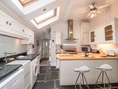 A kitchen with white cabinets two stools at a wooden counter and appliances at Hazeldene in Ambleside