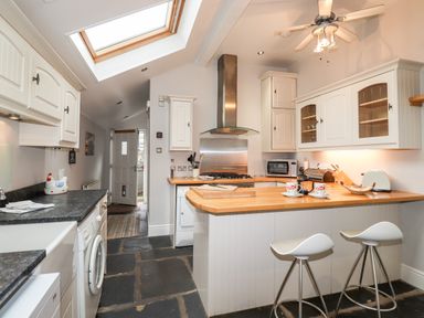 A kitchen with white cabinets wooden countertops bar stools and a skylight at Hazeldene in Ambleside