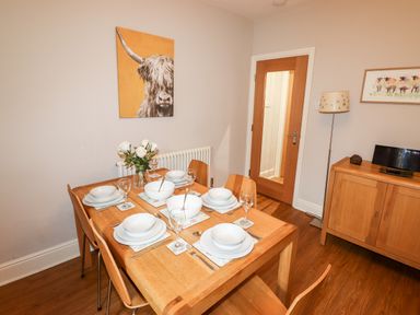 A dining table set with bowls glasses and cutlery in a room with wooden floor a sideboard a floor lamp and animal paintings at Hazeldene in Ambleside
