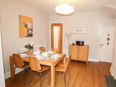 A dining room with a wooden table set for six, wooden chairs, a small cabinet with a television, and two paintings on the walls at Hazeldene in Ambleside
