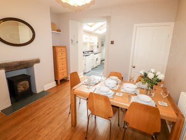 A dining room with wooden table and chairs set with plates bowls glasses and flowers and a view of a kitchen at Hazeldene in Ambleside