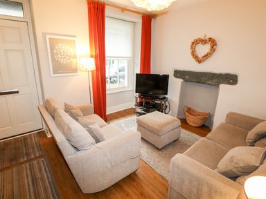 A living room with two sofas a TV on a stand a floor lamp and a window with red curtains at Hazeldene in Ambleside