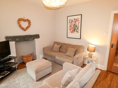 A living room with beige sofas a TV on a stand and a lamp on a side table at Hazeldene in Ambleside