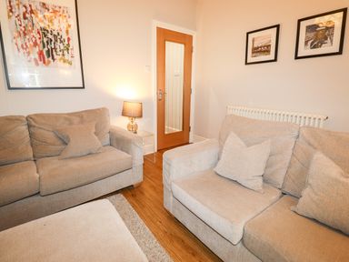 A living room with beige sofas cushions a lamp on a side table wooden flooring and framed pictures on walls at Hazeldene in Ambleside