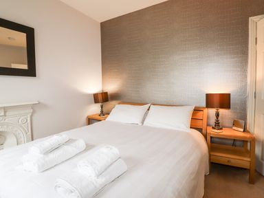 A bedroom with a double bed two bedside tables with lamps and rolled white towels on the bed at Hazeldene in Ambleside