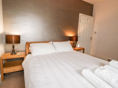 A bedroom with a double bed white linens bedside tables with lamps and folded towels near the foot of the bed at Hazeldene in Ambleside