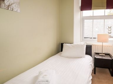 A single bed with white pillow and towel next to a window with a lamp on a bedside table at Hazeldene in Ambleside