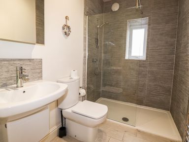 A bathroom with a sink, toilet, walk-in shower with glass panel and window at Hazeldene in Ambleside