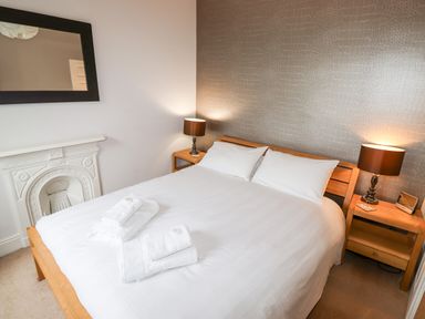 A bedroom with a wooden bed white bedding two bedside tables with lamps a decorative fireplace and a wall mirror at Hazeldene in Ambleside