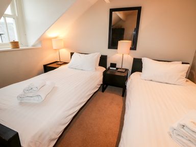 A bedroom with two single beds with white linens bedside tables with lamps and a window at Hazeldene in Ambleside