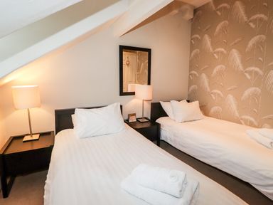 A bedroom with two single beds a bedside table with lamps and a mirror on the wall at Hazeldene in Ambleside