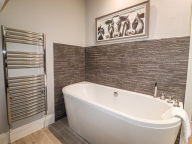 A bathroom with a white bathtub next to a chrome towel radiator and a painting of cows above Hazeldene in Ambleside
