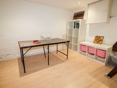 A game room with a table tennis table two paddles white shelves with books and pink bins with a game zone sign at Hazeldene in Ambleside