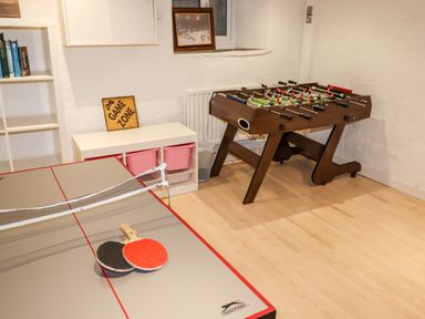 A game room with a ping pong table and foosball table and a shelf with books and bins at Hazeldene Ambleside