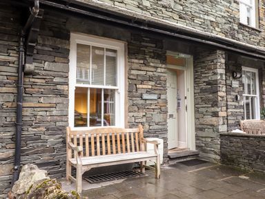 A stone exterior wall with two windows wooden benches and an open door at Hazeldene in Ambleside