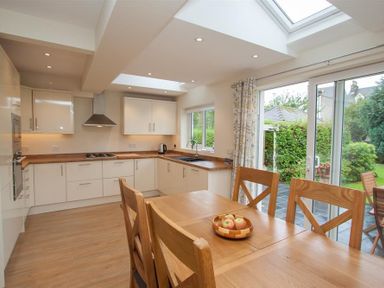 A kitchen with white cabinets wooden countertops a wooden dining table with chairs and a bowl of apples at Fell End in Keswick