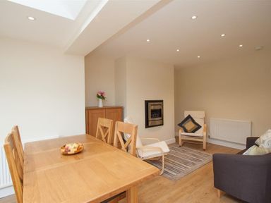A dining area with a wooden table and chairs and a seating area with armchairs and a sofa at Fell End in Keswick
