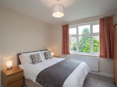 A bedroom with a double bed two bedside tables lamps a window with curtains and a wardrobe at Fell End in Keswick