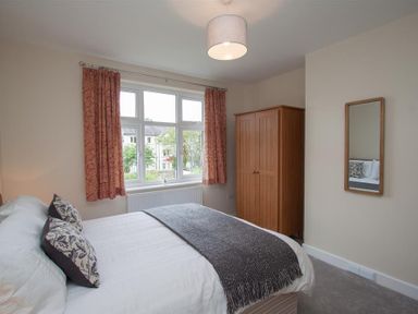A bedroom with a bed with pillows and a throw blanket a wooden wardrobe a mirror on the wall and a window with curtains at Fell End in Keswick