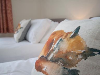 Close up of a pillow with a fox illustration on a bed with white sheets at Fell End in Keswick