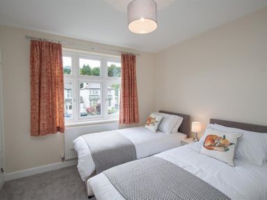A bedroom with two single beds a window with curtains and a bedside table with a lamp at Fell End in Keswick