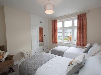 A bedroom with two single beds a built in wardrobe with a mirror a window with red curtains and a chair at Fell End in Keswick