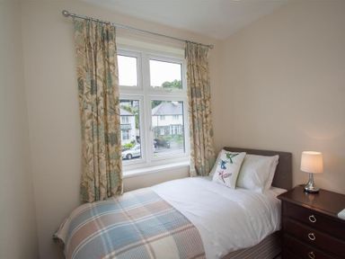 A bedroom with a single bed next to a window with curtains and a bedside table with a lamp at Fell End in Keswick