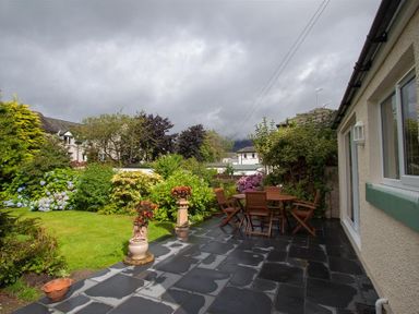 A garden with a patio area featuring a wooden table and chairs surrounded by plants and flowers at Fell End in Keswick