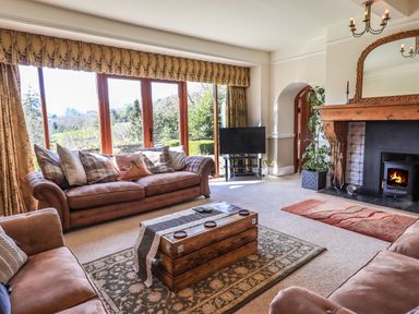 A living room with two sofas a wooden coffee table a fireplace and a television by large windows at The Stables in Ambleside