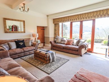 A living room with three sofas a wooden coffee table a rug and large windows at The Stables in Ambleside