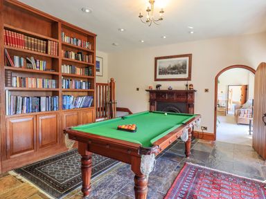 A room with a pool table a wooden bookshelf and a fireplace at The Stables in Ambleside