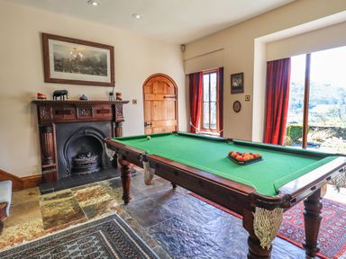 A game room with a pool table near a fireplace and windows at The Stables in Ambleside