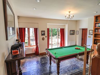 A game room with a pool table red curtains and a wooden bookshelf at The Stables in Ambleside