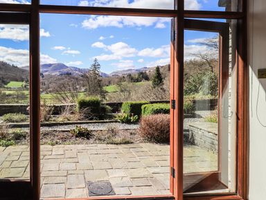 A stone patio with garden and mountain view through open glass door at The Stables in Ambleside