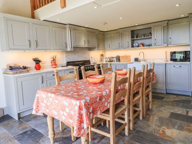 A kitchen with grey cabinets a stove a dining table with wooden chairs and an orange tablecloth at The Stables in Ambleside